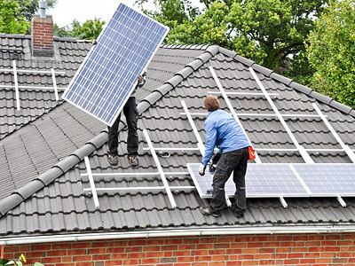 Zwei Monteure installieren Solarpanels auf einem Dach.