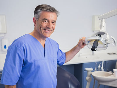 Ein Zahnarzt in einem Behandlungsraum lächelt und hält ein zahnmedizinisches Instrument.